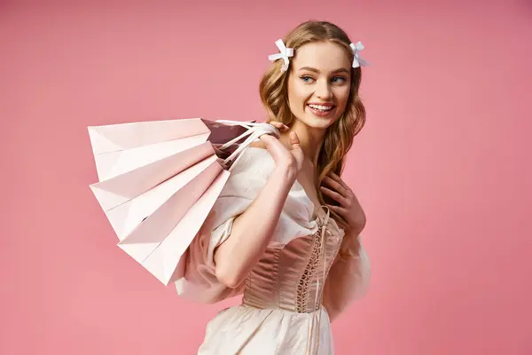 流れる白いドレスの若いブロンドの女性は 穏やかなスタジオの設定で紙袋を巧みに保持しています — ストック写真