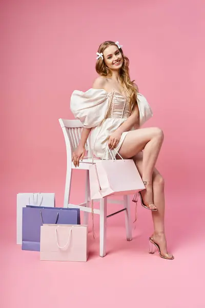 若いブロンドの女性はスタジオの設定でショッピングバッグに囲まれて椅子の上に座るようにスタイルと洗練を排除します — ストック写真