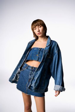 Kısa saçlı genç bir kadın şık bir stüdyo ortamında şık bir kot ceket ve etek giyer..