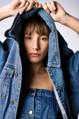 A young woman with short hair joyfully raises her jean jacket over her head in a studio setting. clipart