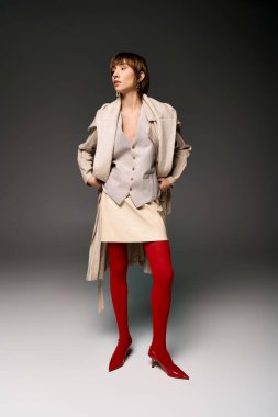 Kısa saçlı genç bir kadın, stüdyo ortamında tayt ve palto giyerek poz veriyor..