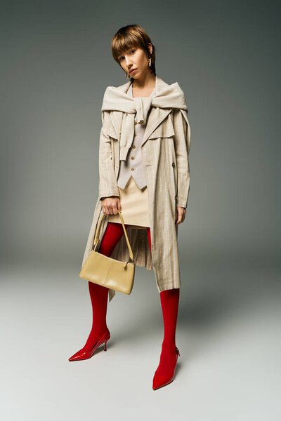 A young woman with short hair, wearing a trench coat, confidently holds a purse in a captivating and mysterious pose.