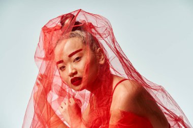 Kırmızı elbiseli çekici bir Asyalı kadın kafasında peçeyle dinamik bir poz veriyor..