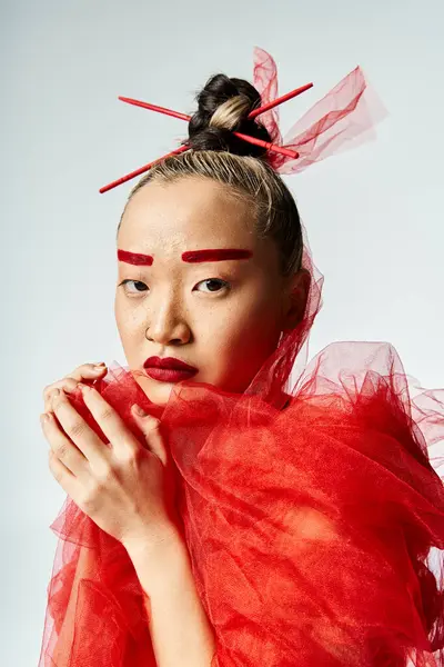 stock image A vibrant Asian woman in a red dress with a red veil around her neck, striking a pose.