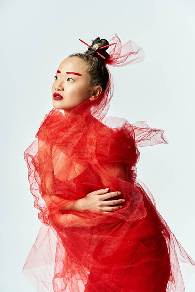 Captivating Asian woman strikes a graceful pose in a vibrant red dress and veil.