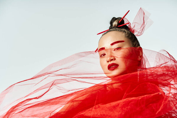 Asian woman striking a pose in crimson dress with veil.