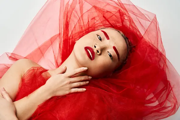 stock image A striking Asian woman in a vibrant red dress and matching lipstick poses confidently.