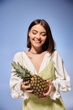 Kumral saçlı genç bir kadın parlak bir stüdyo ortamında taze bir ananas tutuyor..