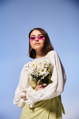 A young woman with brunette hair wearing sunglasses, holding a bouquet of daisies, exuding a serene and vibrant presence. clipart