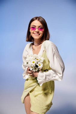Zarif elbiseli esmer kadın stüdyoda canlı bir buket çiçek tutuyor..
