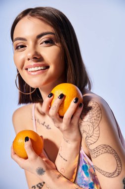 Esmer saçlı genç bir kadın iki portakalı nazikçe elinde tutuyor ve canlı renklerini ve dokusunu gösteriyor..