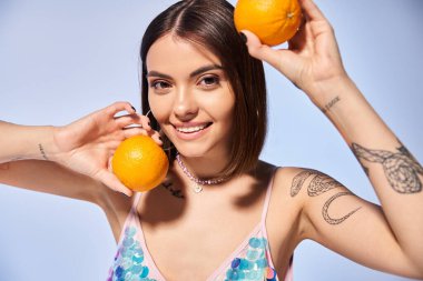 A brunette woman in a studio holding two oranges close to her face, showcasing a connection to nature through vibrant citrus fruits. clipart