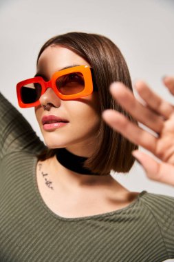 Süslü, esmer, turuncu güneş gözlüğü takan ve stüdyo ortamında yeşil gömlek giyen genç bir kadın..