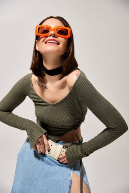 A fashionable young brunette woman confidently wears sunglasses and a stylish skirt in a studio setting. clipart