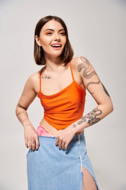 A brunette woman wearing a skirt confidently displaying a tattoo on her arm in a studio setting. clipart