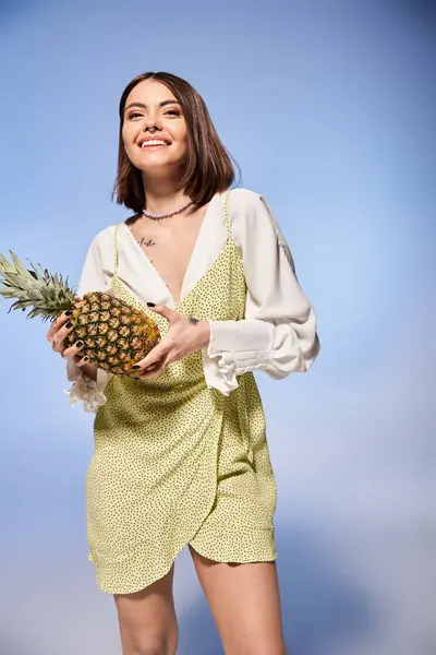 stock image A brunette woman gracefully holding a vibrant pineapple in a stylish dress.