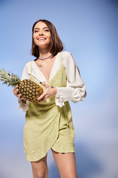 A brunette woman gracefully holding a vibrant pineapple in a stylish dress.