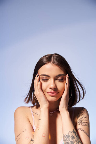Молодая женщина с татуировками и брюнетками, держащая руки к лицу в студии.