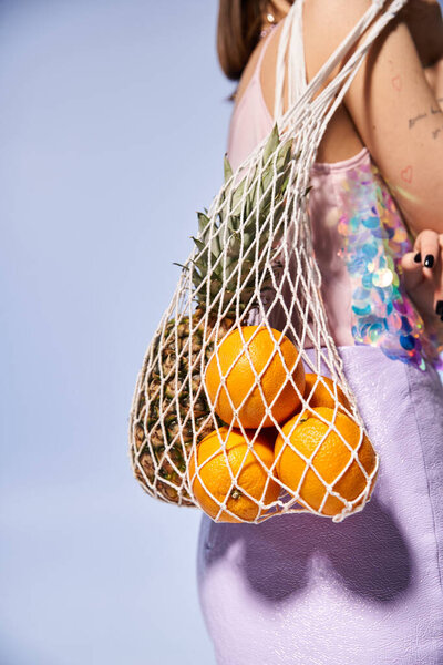 Молодая женщина с брюнетками с радостью держит сумку, полную свежих апельсинов в яркой студии.
