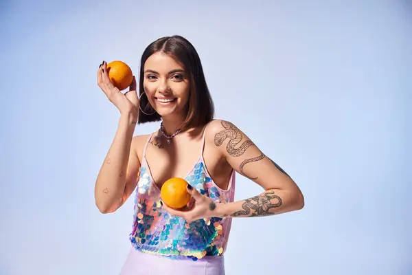 ブルネットの髪を持つ若い女性は スタジオの設定で彼女の手に2つの活気に満ちたオレンジを持っています — ストック写真