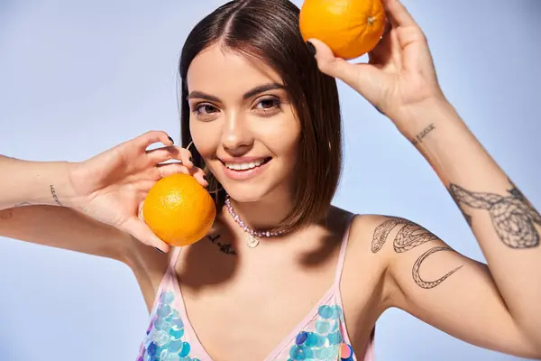 顔の近くに2つのオレンジを持っているスタジオのブルネットの女性は 活気に満ちた柑橘類の果物を通して自然とのつながりを示しています — ストック写真