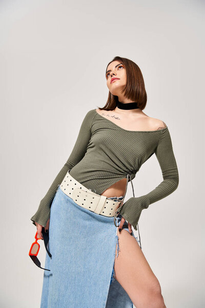 Брюнетка, изящно позирующая в юбке и топе в студии.