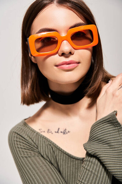 A brunette woman exudes style and confidence while wearing trendy orange sunglasses in a studio setting.