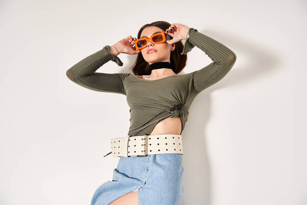 Молодая женщина с брюнетками носит зеленую рубашку и стильные оранжевые солнечные очки в студии.