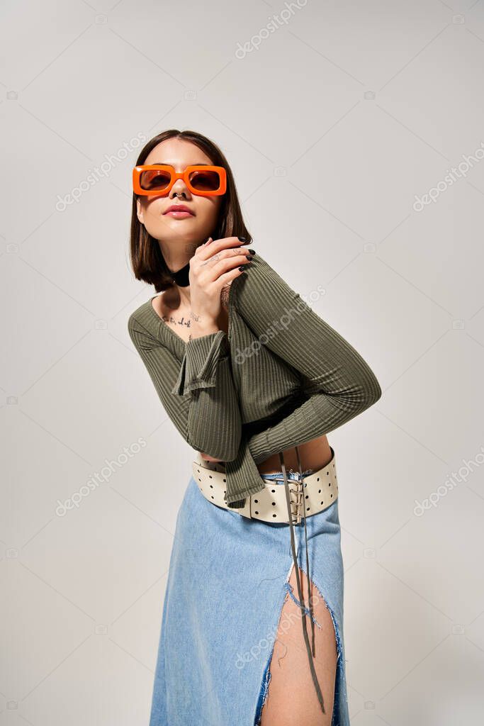 A young woman with brunette hair confidently poses for a picture in a stylish skirt and sunglasses.
