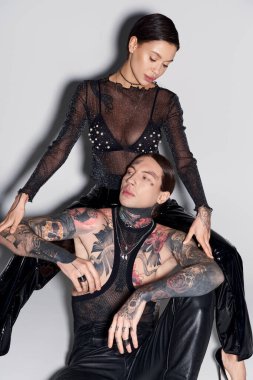 A man with tattoos sitting near woman in a studio setting against a grey background. clipart