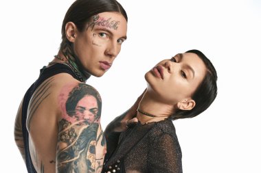 A young stylish couple with arm tattoos embracing in a studio against a grey background. clipart