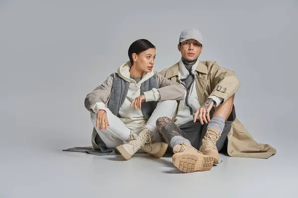 stock image A man and a woman seated on the ground engaged in deep discussion. The woman, in a stylish trench coat, looks attentive.