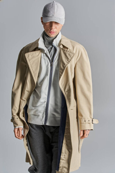 Молодой, татуированный мужчина уверенно стоит в плаще и шляпе, источая атмосферу таинственности и интриги..