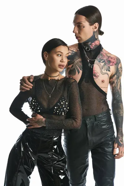 stock image A stylish, tattooed man and woman stand side by side in a studio against a grey background, showcasing their unique look.