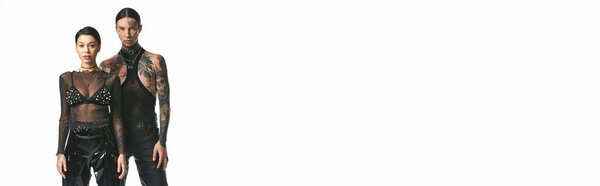 A stylish and tattooed young couple standing together in a studio against a grey background.