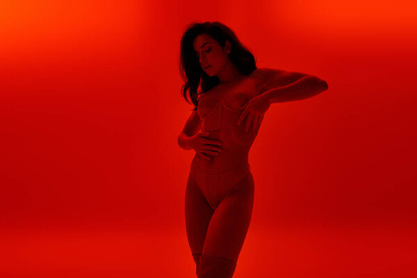 Соблазнительная молодая женщина в нижнем белье стоит в яркой красной комнате.