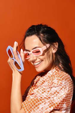Güneş gözlüklü şık bir kadın yüzünün yanında makas tutuyor. Yaratıcılık ve cesur moda seçimleri sergiliyor..