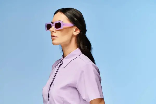 一个戴着太阳镜和紫色衬衫的时髦女人自信地在一个充满活力的蓝色工作室背景下摆姿势 — 图库照片