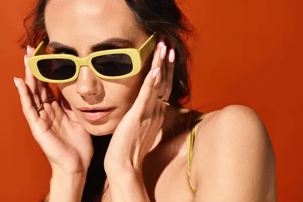 オレンジ色の背景のスタジオでイエローサングラスを着用したファッショナブルな女性 — ストック写真
