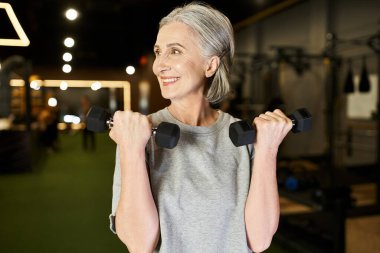 Güzel görünümlü, rahat giyimli spor kadın spor salonunda halterlerle aktif egzersiz yapıyor.