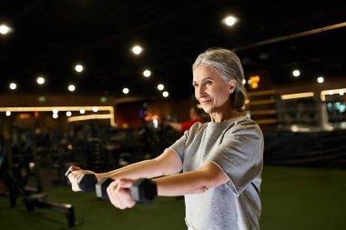 Spor giyim bölümünde spor salonundayken halterlerle antrenman yapan güzel, neşeli atletik bir kadın.