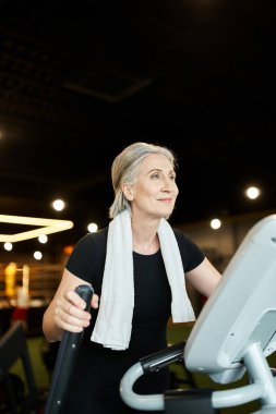 Siyah tişörtlü çekici, son sınıf sporcusu eliptik antrenör üzerinde aktif egzersiz yapıyor.