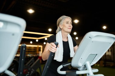 Sportif, son sınıf öğrencisi, spor salonunda omuzlarında havluyla antrenman yapıyor.