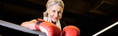 Yüzük üzerinde egzersiz yapan ve kameraya gülümseyen, boks eldivenli hoş, son sınıf güzeli bir kadın.