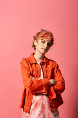 Parlak pembe bir duvarın önünde kendine güvenen kızıl saçlı şık bir kadın..