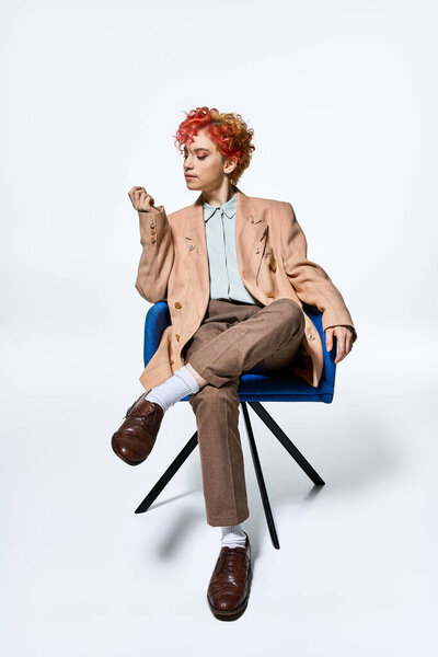 Необыкновенная женщина с яркими рыжими волосами расслабляется на ярком синем стуле.