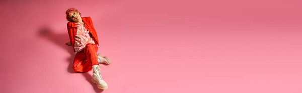 Блестящая женщина в красном костюме лежит на мягкой розовой поверхности.