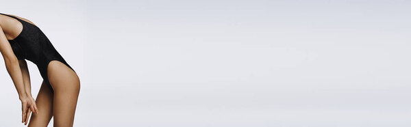 Стильная молодая женщина изящно наклоняется в черном купальнике.