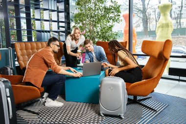 Bir şirket gezisi sırasında otel lobisinde dizüstü bilgisayarla masa etrafında çalışan çok kültürlü iş arkadaşları..