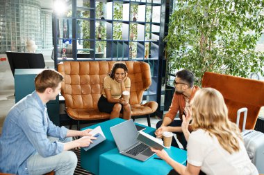 Bir otel lobisindeki çok kültürlü meslektaşlar, gündelik giysiler içindeki çeşitli iş adamları, dizüstü bilgisayarlarla bir masanın etrafında oturuyorlar..